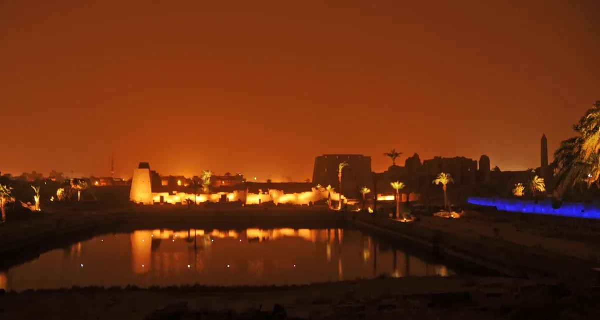 The sacred lake at Karnak lit up at night with the temple walls reflected in the water, seen on a Valley of the Kings tour